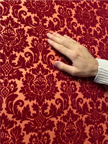 Main touchant un papier peint en relief aux motifs baroques rouges lors d'une visite sensorielle pour malvoyants.